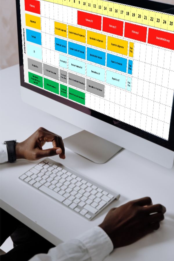 Eine Person betrachtet einen Einreihungsplan auf einem Desktop-Bildschirm. Die farbig codierte Tabelle zeigt verschiedene Jobrollen und deren zeitliche Verteilung. Die Felder in der Tabelle sind mit Jobtiteln und -bereichen gefüllt und nach Wochentagen organisiert.